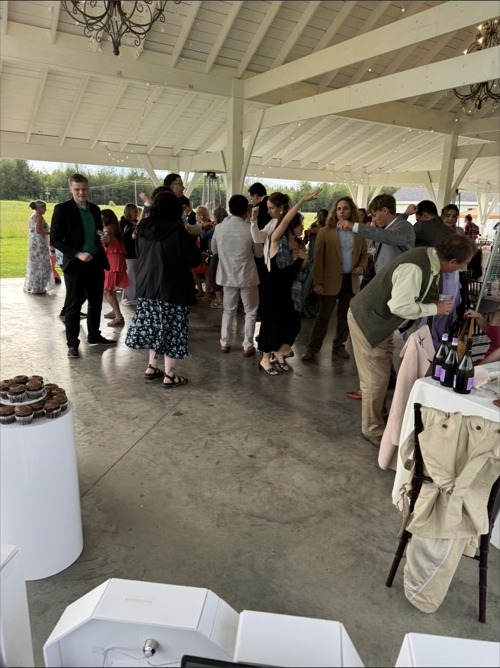 Wedding guests gathered on a pavilion dancefloor with the DJ booth visible