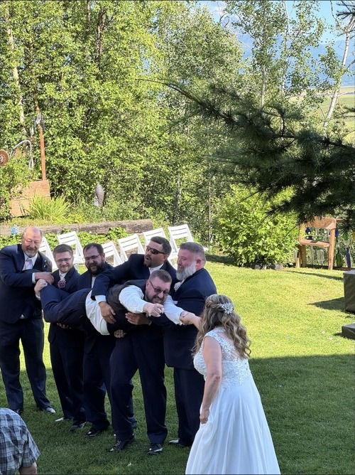 Wedding party playfully holding the groom while the bride looks on